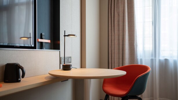 A modern hotel room with a round table, a red and blue chair, a coffee maker, and a lamp. - Holiday Inn Express Guangzhou Panyu by IHG (Guangzhou)