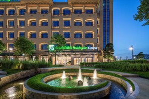 Ein Holiday Inn Express Hotel mit einem begrünten Brunnen davor.