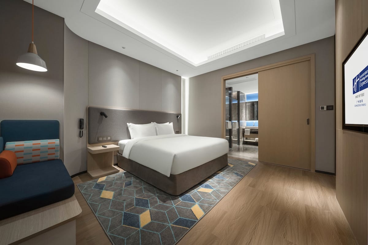 A modern hotel room with a large bed, a desk, a chair, and a sofa.