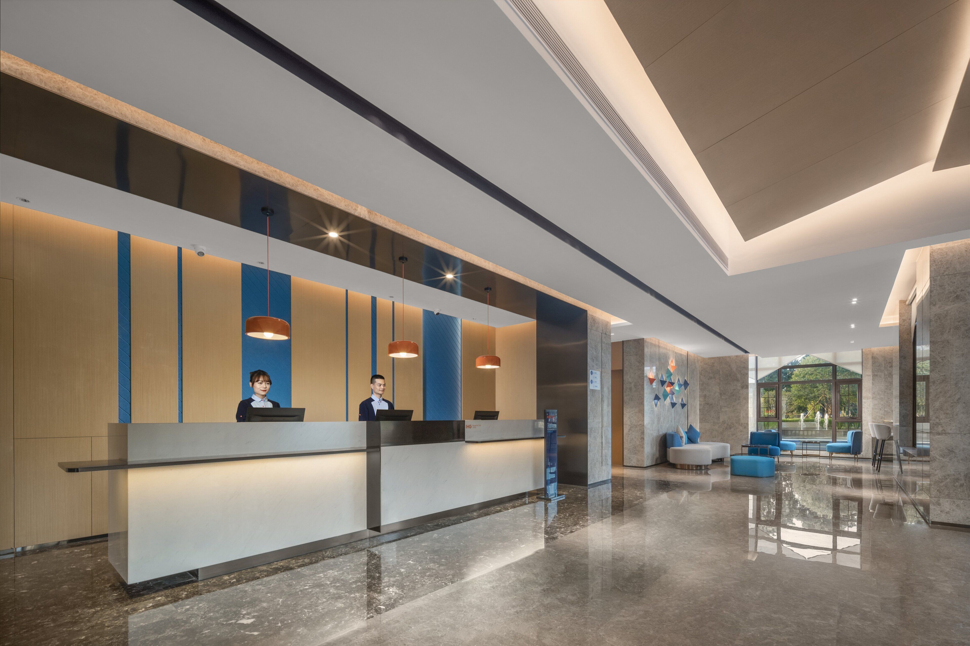 A modern hotel lobby with a reception desk, seating area, and large windows offering a view of the outdoors.