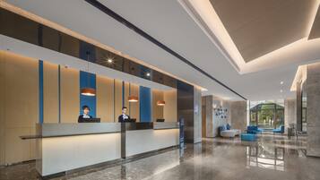 A modern hotel lobby with a reception desk, seating area, and large windows offering a view of the outdoors.