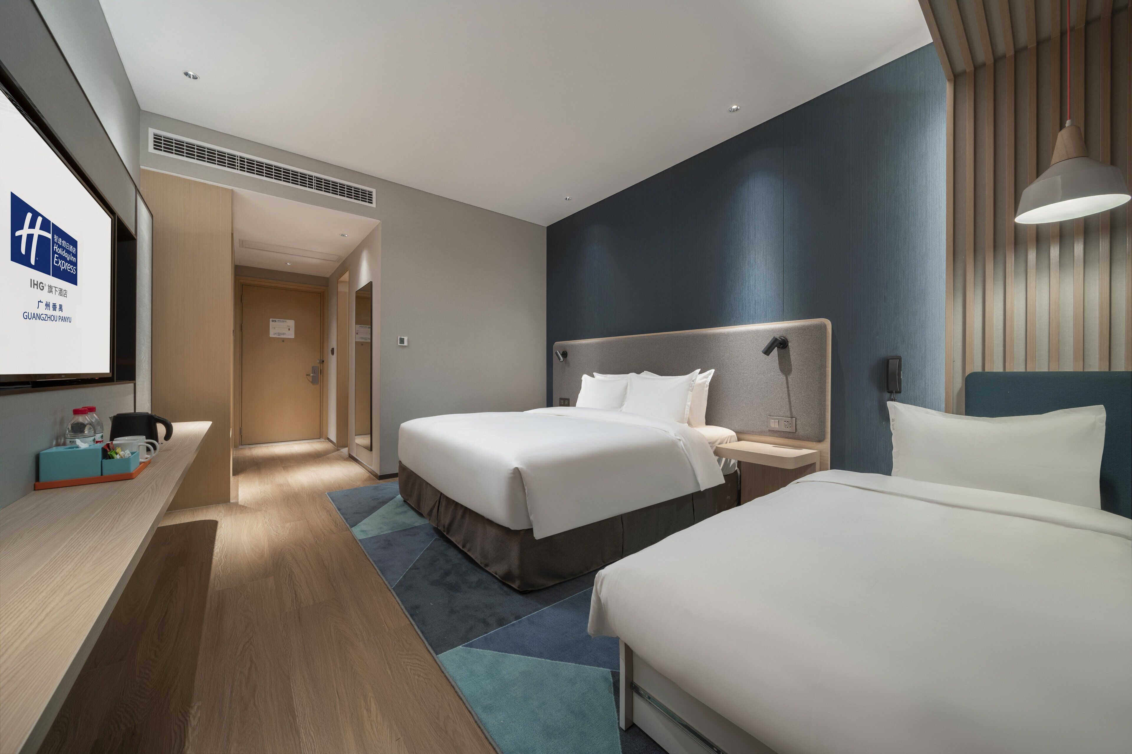 Una habitación de hotel moderna con dos camas, un escritorio y una pantalla grande que muestra el nombre del hotel.