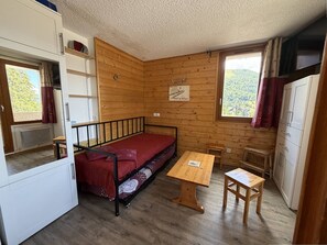 A compact room with a bed, a small table, and a kitchenette area.