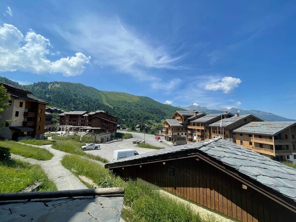 A mountain village with traditional wooden buildings, a dirt road, and a clear blue sky.