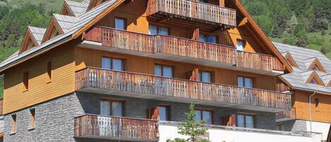 A multi-story hotel with balconies, stone facade, and a car parked in front.