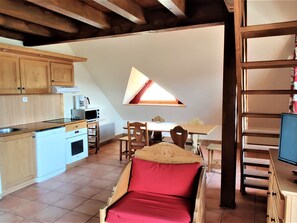 A compact kitchen with a dining area, a loft bed, and a small window.
