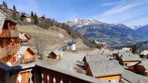 Un pueblo de montaña con edificios de madera, una carretera sinuosa y montañas nevadas al fondo.