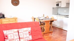 Een gezellige woonkamer met een rode bank, een houten eettafel en een keuken met witte apparaten.