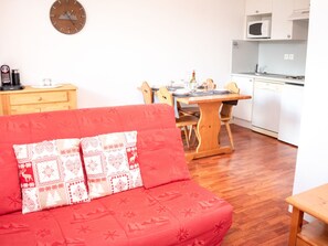 Ein gemütlicher Wohnbereich mit einem roten Sofa, einem Holzesstisch und einer Küche mit weißen Geräten.