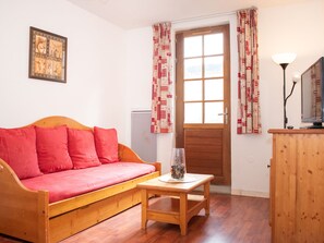 A cozy room with a wooden sofa, a small wooden table, a lamp, and a door with patterned curtains. - Charming 2 Rooms in Vignec with Terrace, 6 Pers (Vignec)