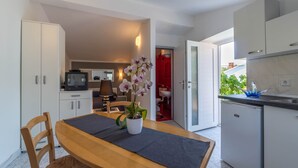 Una cocina moderna con armarios blancos, una mesa de comedor de madera y un jarrón con flores, y una puerta roja que da al baño.