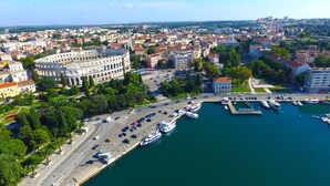 Vista aérea de una ciudad con un edificio histórico destacado, un puerto deportivo con barcos y una combinación de edificios residenciales y comerciales.