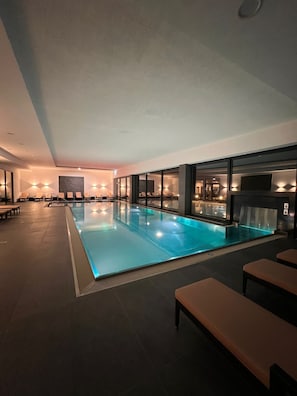 An indoor swimming pool with a tiled floor, benches, and wall-mounted lights. - Rebhans Business und Wellness Hotel (Stockheim)