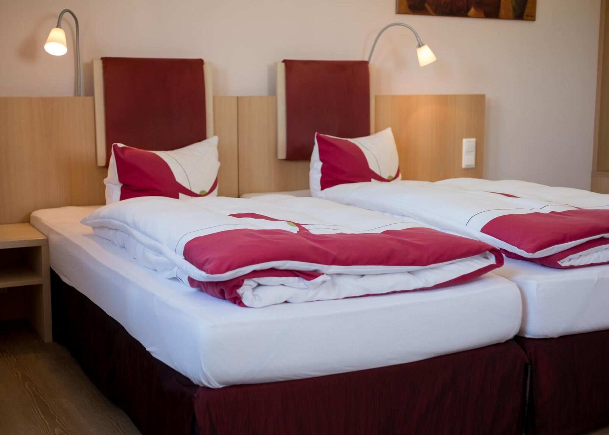 Una habitación de hotel con dos camas, cada una con ropa de cama roja y blanca, y dos lámparas fijadas a la pared.