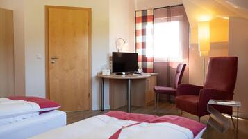 Habitación de hotel con dos camas, un escritorio con computadora, una silla y una ventana con cortinas.