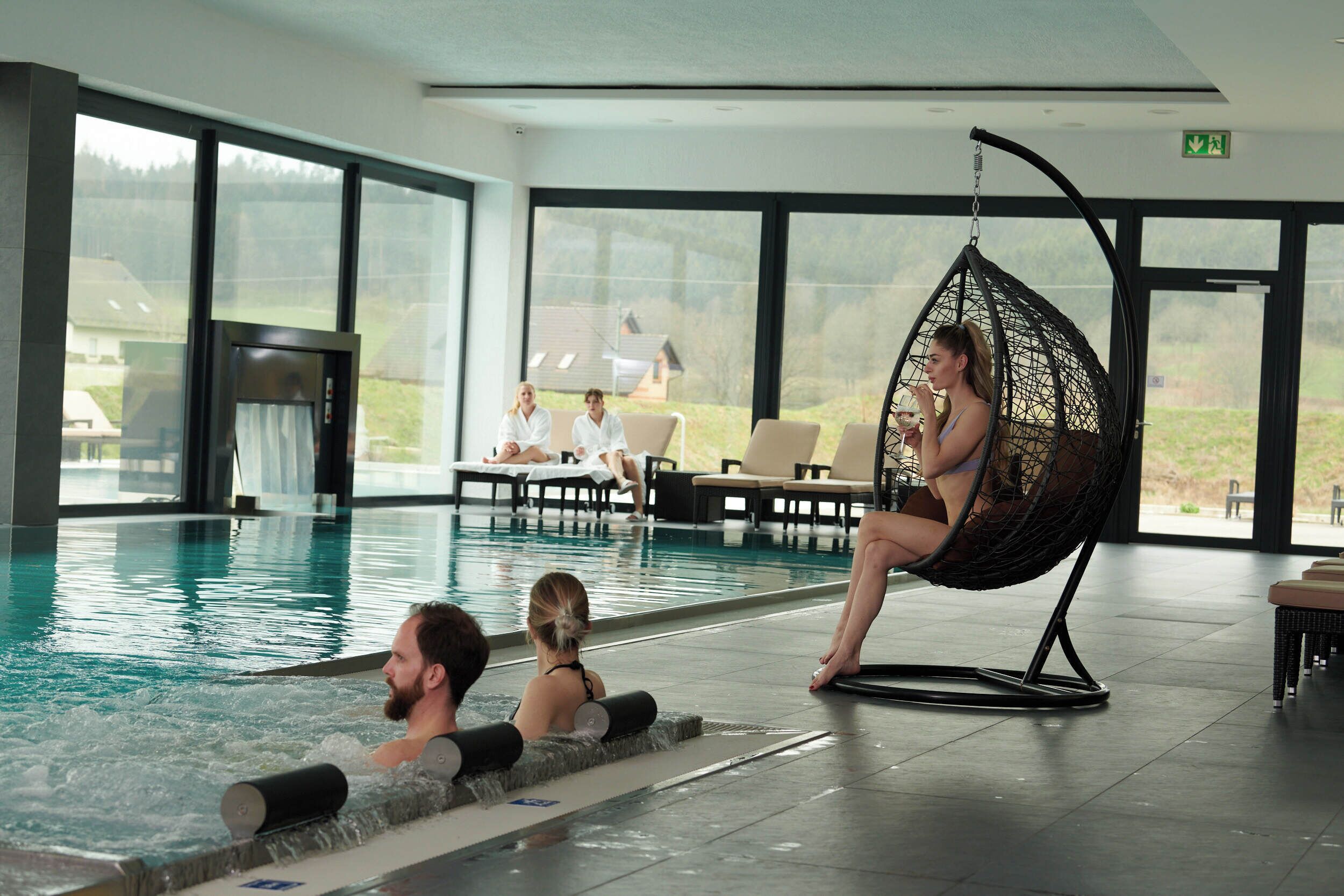 Un espace piscine comprenant un jacuzzi, des chaises longues et un fauteuil suspendu.
