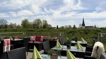 Un espace extérieur aménagé avec des tables et des chaises, une vue sur une église et de la verdure en arrière-plan.