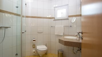 A bathroom with a glass-enclosed shower, a toilet, a sink with a granite countertop, and a window providing natural light.