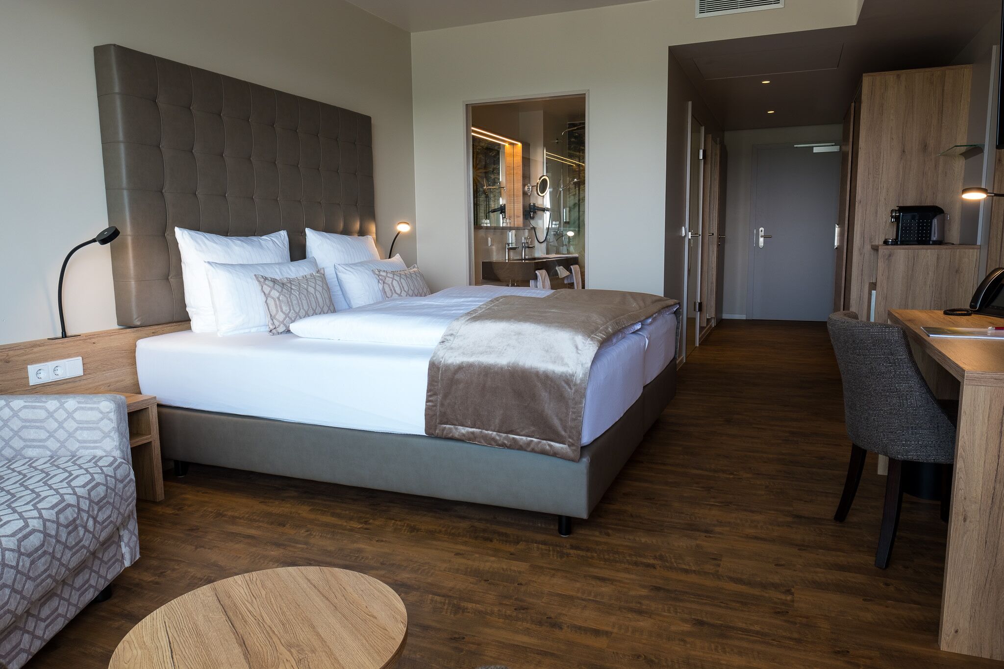 A modern hotel room with a large bed, a desk, and a mirror.