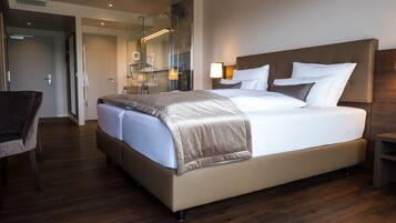 Habitación de hotel moderna con una cama grande, una silla, un escritorio y un baño con cabina de ducha de vidrio.