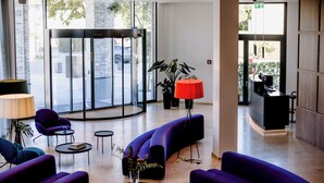 A modern lobby with purple sofas, a reception desk, and a large glass door leading outside. - THE FLAG Meiller Gärten (Munich)