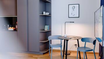 Une pièce moderne avec un meuble gris, une chaise bleue, une petite table ronde et un tableau encadré au mur.