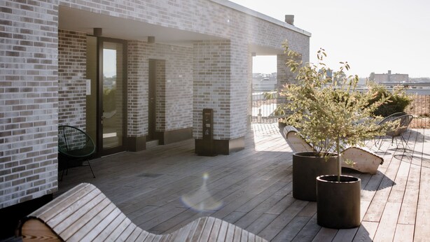 A rooftop terrace with a brick wall, a wooden deck, and a lounge chair. - THE FLAG Meiller Gärten (Munich)