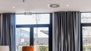A modern hotel room with a large window, a sofa, two armchairs, a floor lamp, and a small table. - THE FLAG Meiller Gärten (Munich)