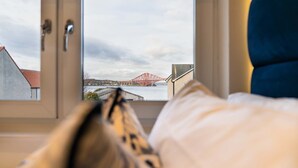 Ein Bett mit Blick auf eine rote Brücke und Gebäude durch ein Fenster.