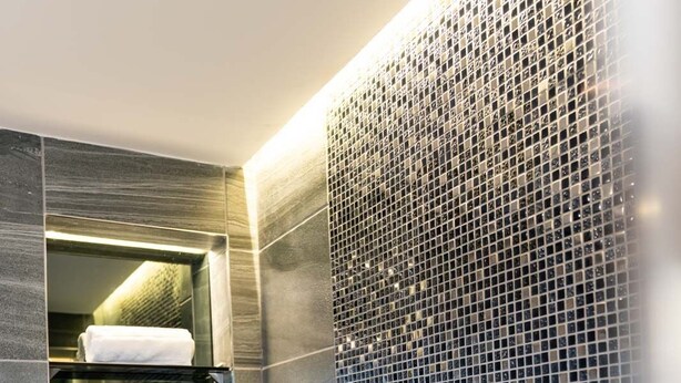 Ein modernes Badezimmer mit einer Glasregaleinheit, einer gefliesten Duschwand und einer weißen Badewanne.