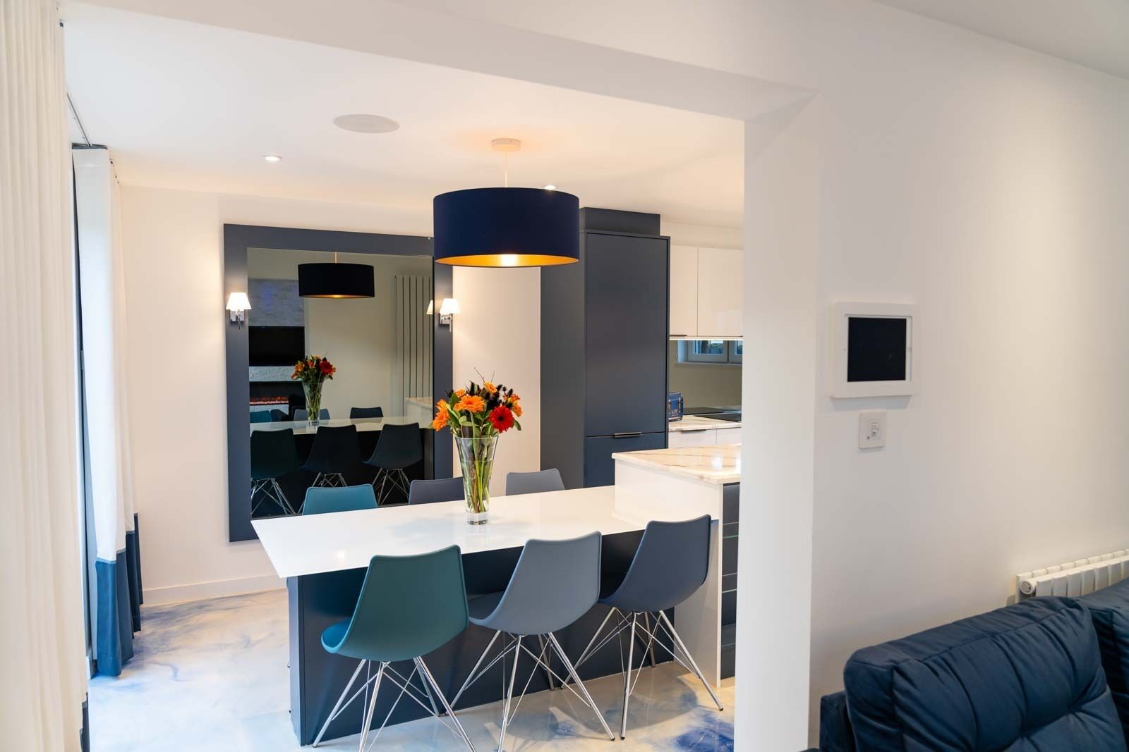 A modern dining area with a white table, blue chairs, and a vase of flowers.