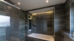 Ein modernes Badezimmer mit einer freistehenden Badewanne, dunkel gefliesten Wänden und einer Duschkabine aus Glas.