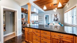 Une cuisine moderne avec des meubles en bois, un plan de travail en granit, un éclairage suspendu et une grande fenêtre équipée de stores.
