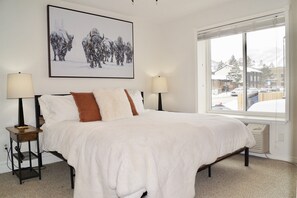 Relax in this serene bedroom with a large bed, nightstand, and framed artwork, offering a view of the surrounding area.