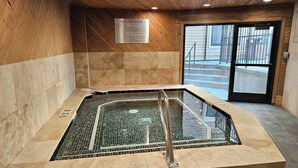 Una bañera de hidromasaje con una escalera metálica, rodeada de paredes de azulejos y un techo de madera.