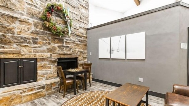 Una habitación con chimenea de piedra, un comedor con sillas, una mesa de centro redonda y una pared gris con un cuadro enmarcado.