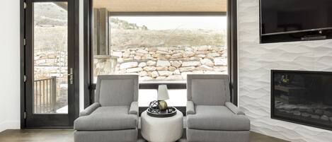 Una sala de estar moderna con dos sillones tapizados, una mesa de centro redonda y un televisor de pantalla plana montado en la pared.