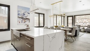 A modern kitchen with a marble island, large windows, and a dining area with a stone wall view. - Stunning! Walk to lift - Beautiful pool complex (Park City)