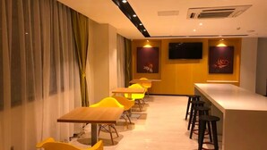 Un restaurant moderne avec des chaises et des tables jaunes, un coin bar avec des tabourets et des œuvres d’art accrochées aux murs.
