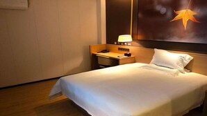 Une chambre d’hôtel avec un lit bien fait, un bureau avec une lampe et un grand tableau accroché au mur.