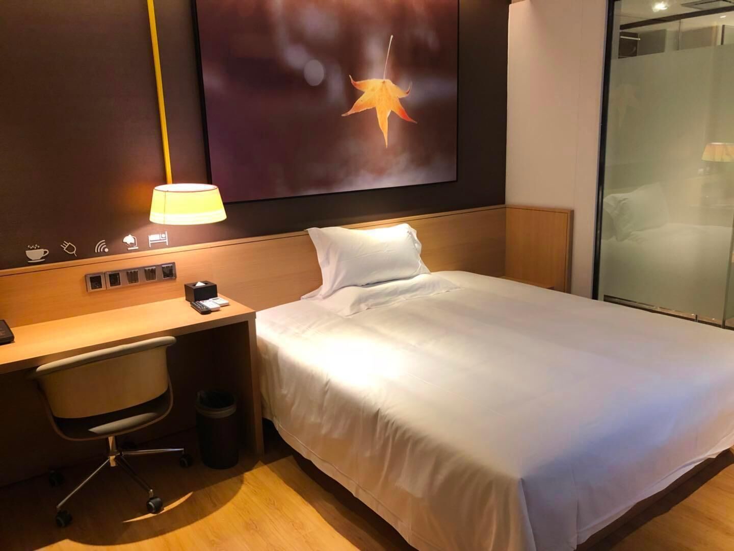 Ein Hotelzimmer mit einem Bett, einem Schreibtisch mit Lampe, einem Sessel und einem Mülleimer.