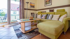 A cozy living room with a green sofa, a wooden coffee table, and a view through a sliding glass door to the outside. - Waldstr. 32 Whg. Wa32-04 - Wa32-04 (Kühlungsborn)