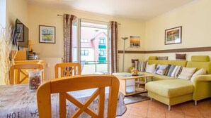 A cozy living room with a green sofa, wooden chairs, a coffee table, and a dining table with a vintage menu. - Waldstr. 32 Whg. Wa32-04 - Wa32-04 (Kühlungsborn)