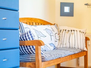 A wooden bench with striped cushions and a dolphin pattern pillow, positioned next to blue storage units.