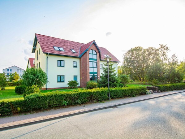 A two-story residential building with a red-tiled roof, large windows, and a well-maintained garden.