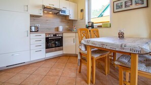 A compact kitchen with white cabinets, a built-in oven, a microwave, and a window providing natural light. - Waldstr. 32 Whg. Wa32-04 - Wa32-04 (Kühlungsborn)