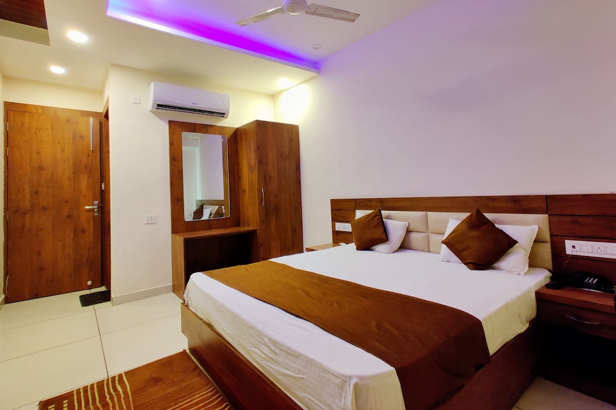 Habitación de hotel con una cama grande, armario de madera, ventilador de techo y aire acondicionado integrado.