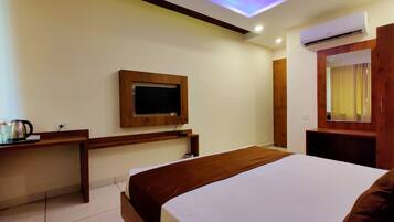 A hotel room with a bed, a TV mounted on the wall, an air conditioning unit, a wooden desk, and a mirror.