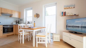 Ett modernt kök med träskåp, ett matbord med stolar, en TV på ett TV-bord och ett stort fönster.