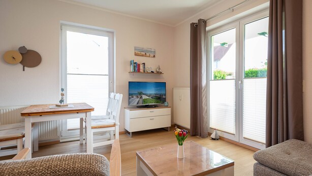 Ett modernt vardagsrum med ett träbord, en vit soffa och en tv.
